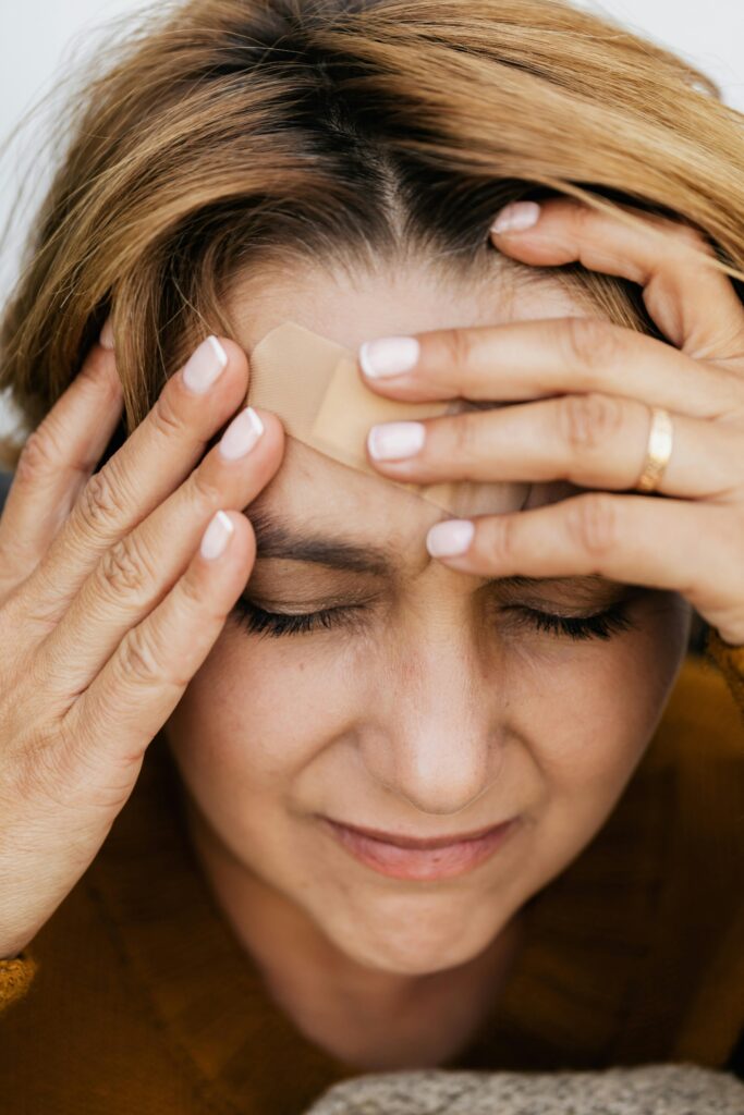 Woman with eyes closed, holding head with a band aid on forehead, expressing pain.